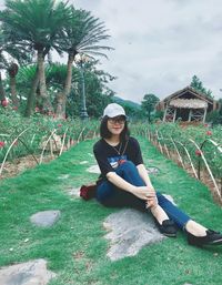 Portrait of smiling young woman sitting on field in public park