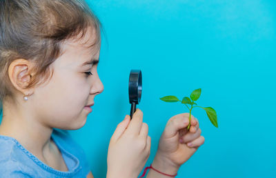 Side view of girl looking at leaves through magnifying glass against blue background