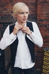 Portrait of young man standing against brick wall