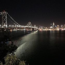 Illuminated bridge over river against sky at night