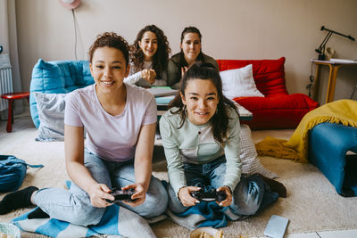 Happy female friends playing video game in living room at home