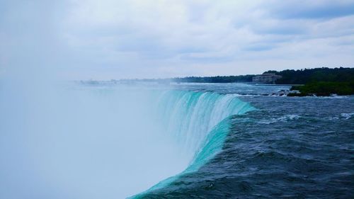 Scenic view of waterfall against cloudy sky