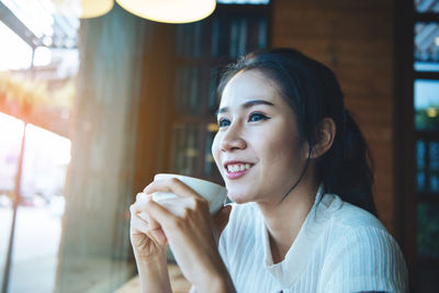 Close-up of smiling young woman looking away while having coffee at cafe