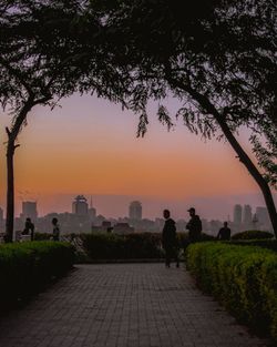 People on sidewalk in city against sky during sunset