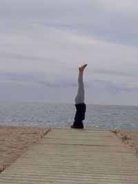 Full length of woman practicing headstand at beach against sky