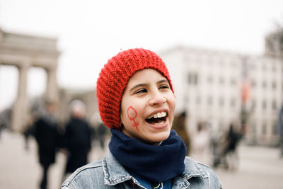 Girl in red cap smiling with face painted with female symbol