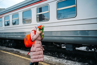 Girl on the platform of the station with a red backpack and a bouquet of tulip flowers