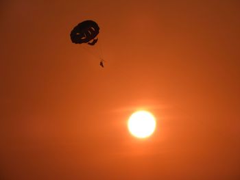 Low angle view of people paragliding against sky during sunset
