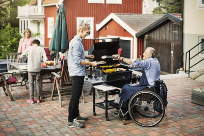 Disabled man serving barbecued food to son at yard