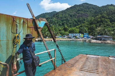 Man standing on boat against trees and mountains against sky