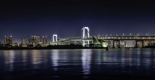 Illuminated bridge over river with city in background