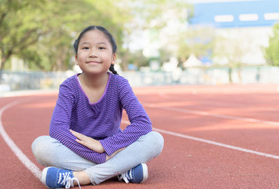 Portrait of smiling girl sitting on running track