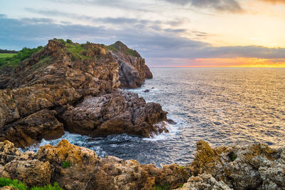 Rocks on sea shore against sky during sunset