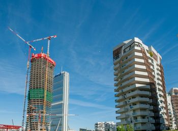 Low angle view of crane by building against blue sky