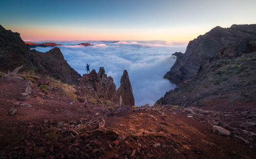 Back view of anonymous male traveler standing with outstretched arms on rocky hill in highlands and enjoying amazing view of clouds