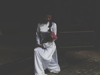 Full length of young woman holding flower while sitting indoors