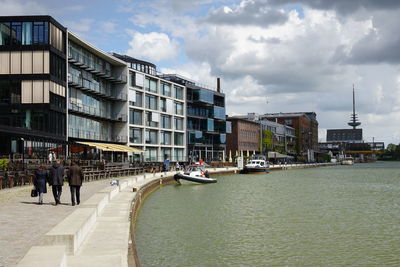 Rear view of friends walking on promenade by canal against fernmeldeturm munster