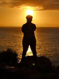 Silhouette man looking at sea against sky during sunset