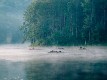 Group of people boating on lake by forest against clear sky