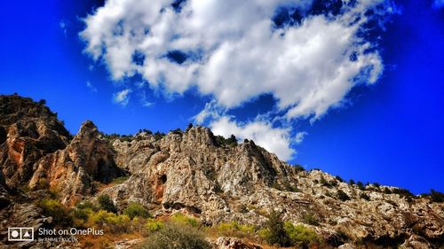 Low angle view of rocky mountain against blue sky