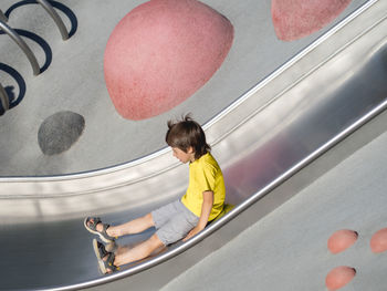 Boy with his eyes closed rides down a metal slide on modern children's sports and playground. 