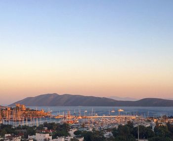 Cityscape by sea against clear sky during sunset