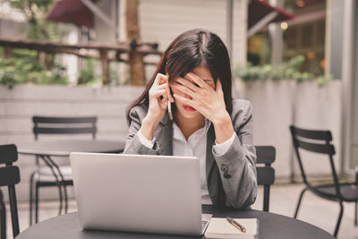 Tensed businesswoman talking on mobile phone at table in cafe