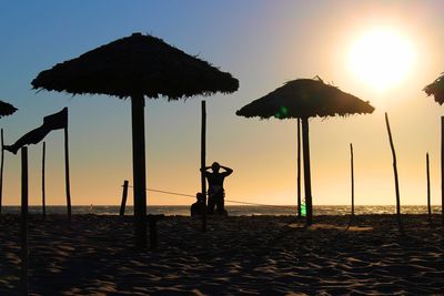 Rear view of silhouette people and sunshades at beach against sky during sunset