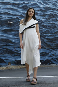 Full length portrait of young woman standing against patterned wall on street