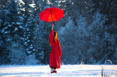 Rear view of woman with umbrella walking on snow covered field