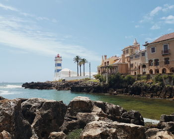 Lighthouse by sea against buildings