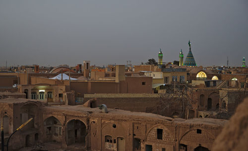 Traditional buildings and mosque with minarets in city in desert against clear sky at sunset