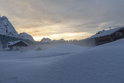 Snow covered houses and mountains against sky during sunset