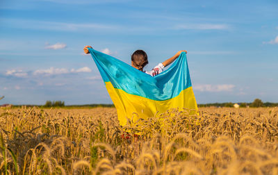 Portrait of woman with arms outstretched standing on field against sky