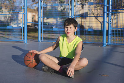 Portrait of boy holding basketball while sitting in court
