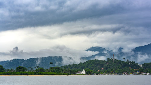 Scenic view of cloudy mountains against sky with ocean in front