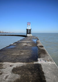 Lighthouse by sea against clear blue sky