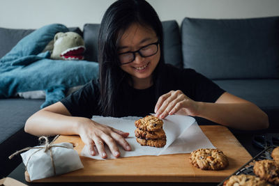Smiling woman wrapping cookie in paper at home