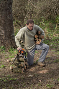 Man carrying logs while kneeling in forest