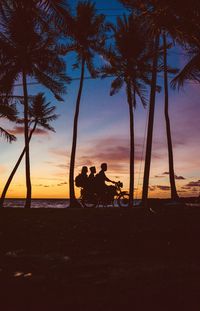 Silhouette people sitting on beach against sky during sunset