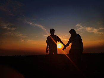 Silhouette men standing against orange sky during sunset