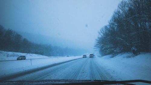 Cars on snow covered street seen through windshield