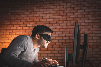 Young man using mobile phone against brick wall