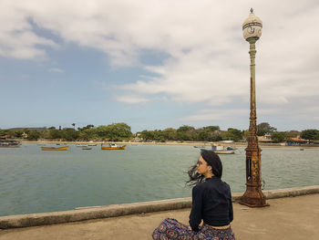 Rear view of woman sitting on boat in river against sky