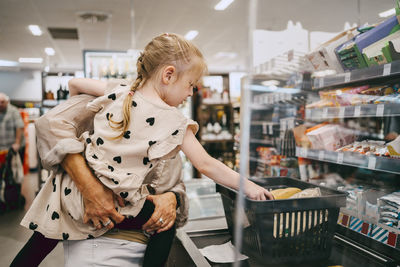 Senior woman carrying granddaughter at checkout counter in supermarket