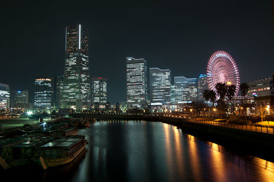 Illuminated buildings and ferris wheel by river at night