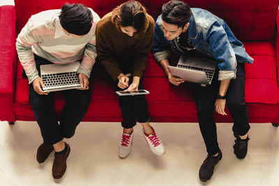 High angle view of business people working over technologies while sitting on sofa in office