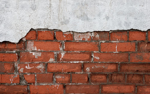 Full frame shot of old red brick wall with damaged grey plaster layer