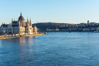 View of buildings by river against sky in city