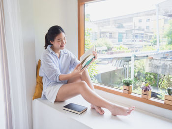 Side view of a smiling young woman sitting on window